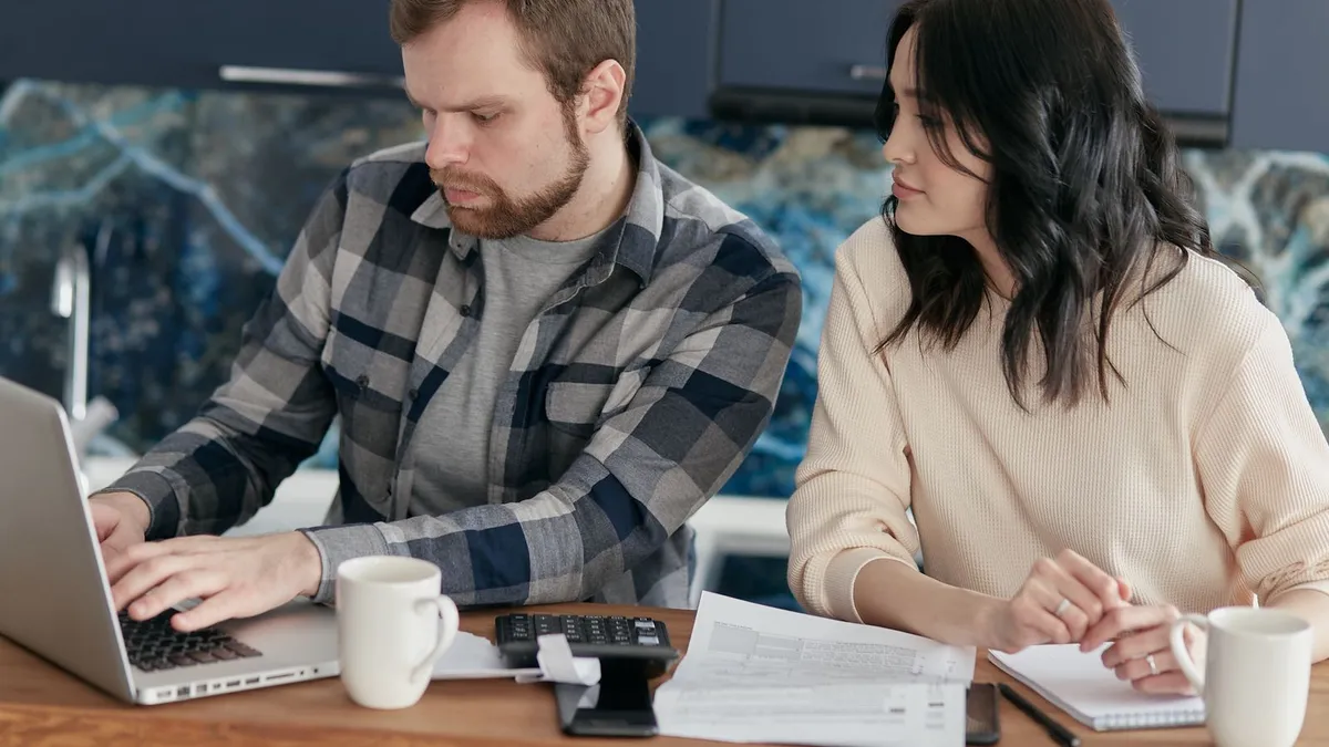Man at a kitchen table reviewing installment loan payments on a laptop
